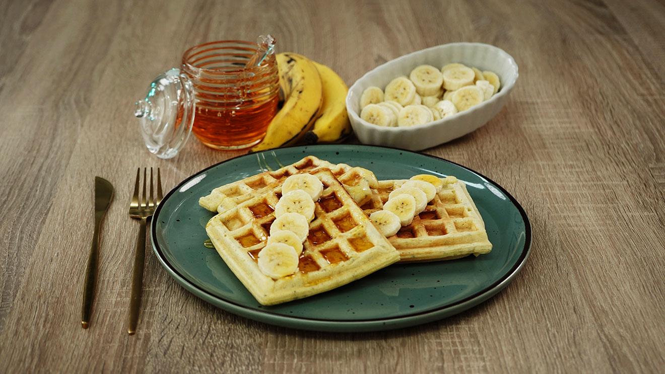 Waffles dourados servidos com banana, mel e uma bebida, fotografia do livro de receitas